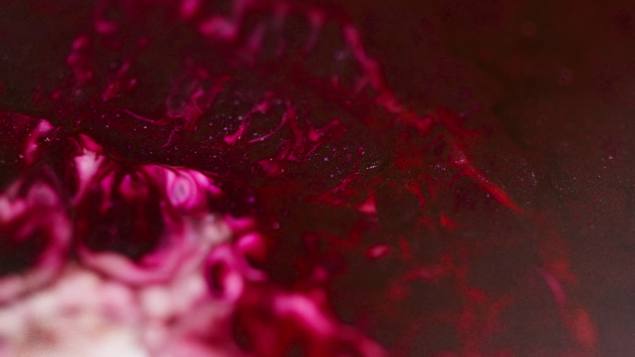 Macro shot of red, pink, and burgundy inks moving and bubbling across the surface, creating abstract fluid patterns