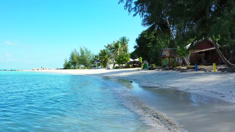 Quiet-exotic-beach-with-white-sand-under-palm-trees-near-bar-restaurants-with-sea-view-on-a-bright-blue-sky-background-in-Myanmar