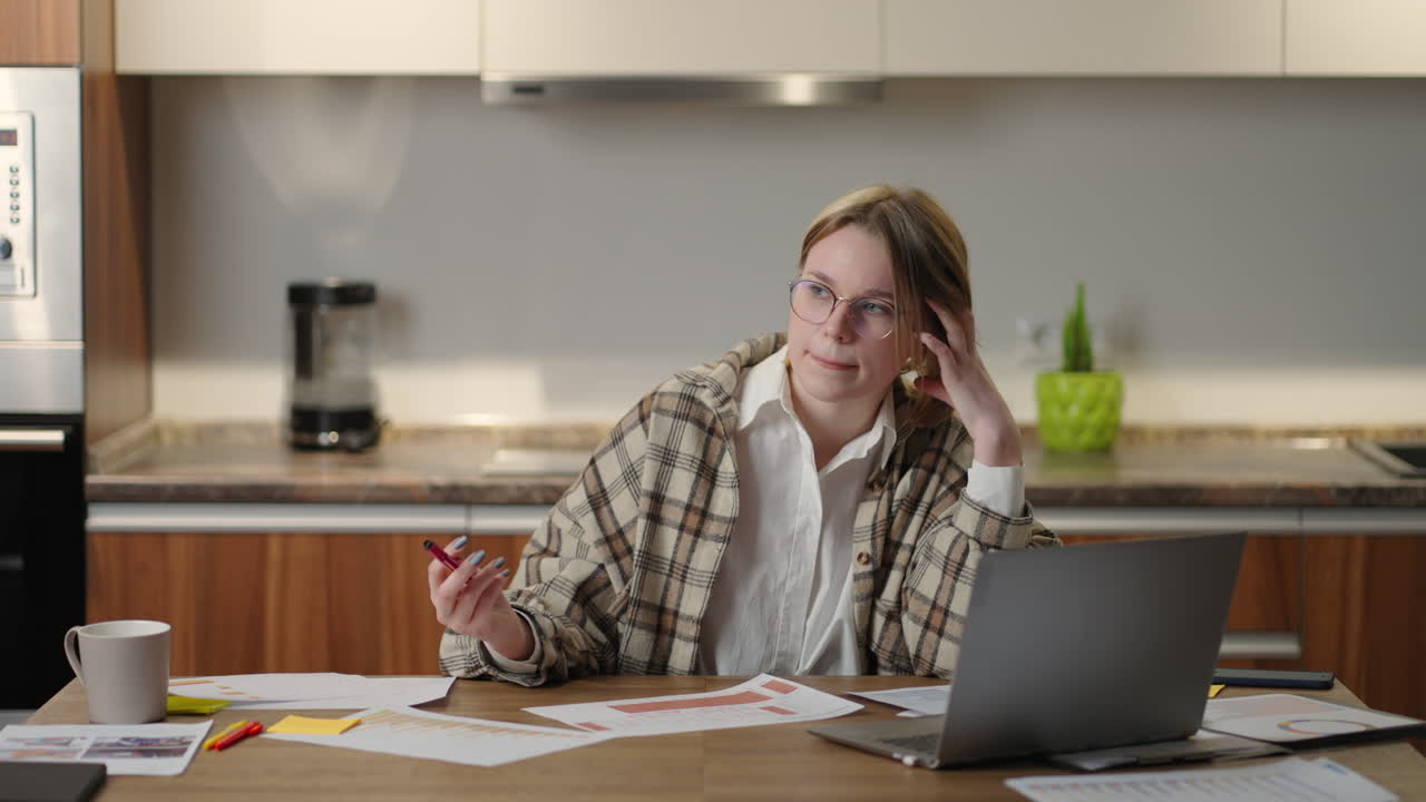 Pensive a woman with glasses working on financial documents sitting at her workplace using a laptop application looks focused completing a task preparing checking a report on a fruitful working