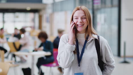 smiling female college student talking on mobile phone in busy communal campus building