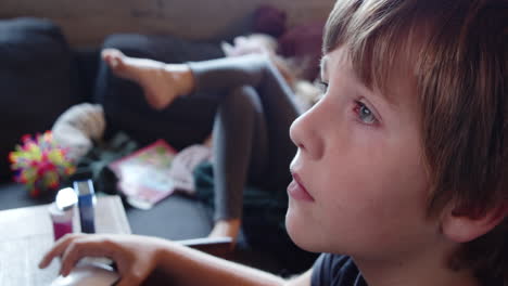 close-up of the face of a boy sitting concentrated in front of a computer and a girl on a couch who is bored