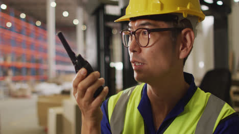 Asian-male-worker-wearing-safety-suit-with-helmet-talking-in-warehouse