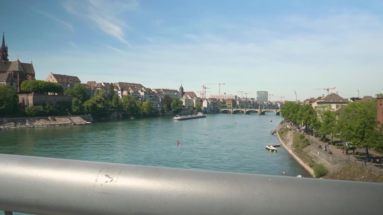 Panoramica verso l'alto da un cartello di divieto di tuffarsi dal ponte a un panorama luminoso e soleggiato del fiume Reno a Basilea, con cielo azzurro limpido, barche e un'atmosfera cittadina calma