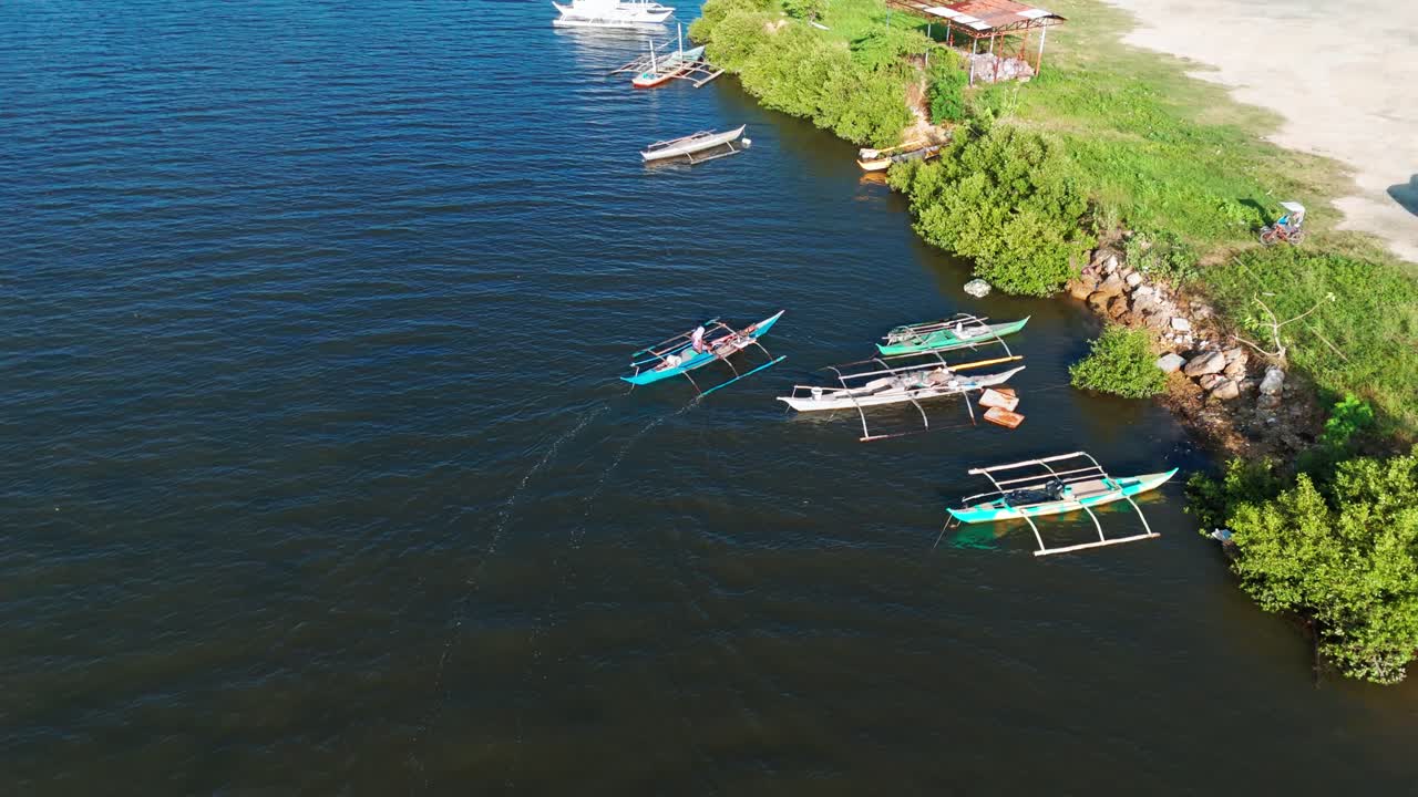 Aerial view of traditional Filipino bangkas docked near a fishing village, with lush mangroves, calm waters, and daily coastal life captured in daylight