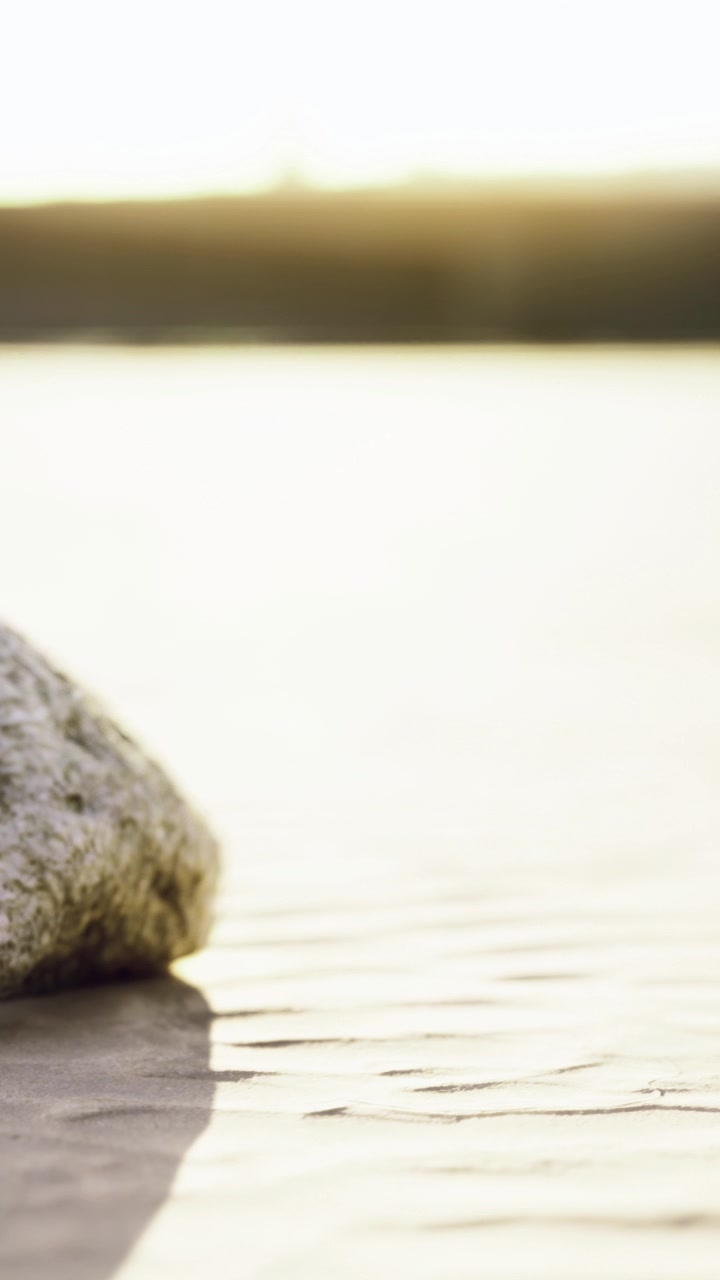 Una roccia si trova sulla sabbia bagnata in spiaggia durante il tramonto sull'oceano.