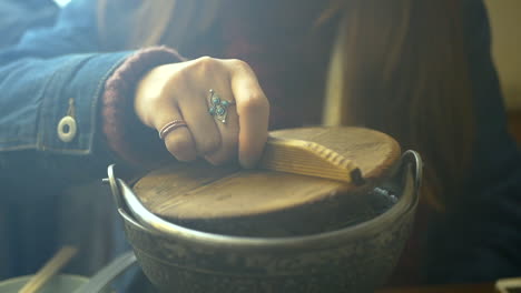 a young woman taking the lid off of a traditional bowl of steaming yuba noodle soup