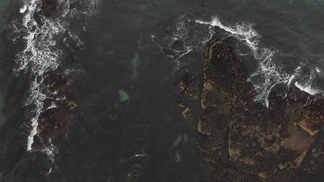 aerial view of dark green water breaking over rocks