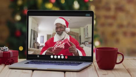 Hombre-Afroamericano-Mayor-Disfrazado-De-Santa-En-Videollamada-En-Computadora-Portátil,-Con-árbol-De-Navidad