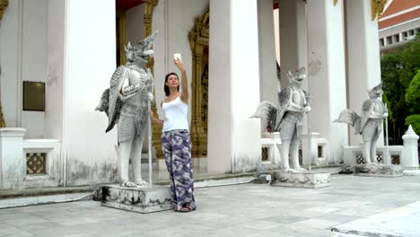 una mujer hace una selfie en un teléfono inteligente junto a una estatua mitológica de piedra
