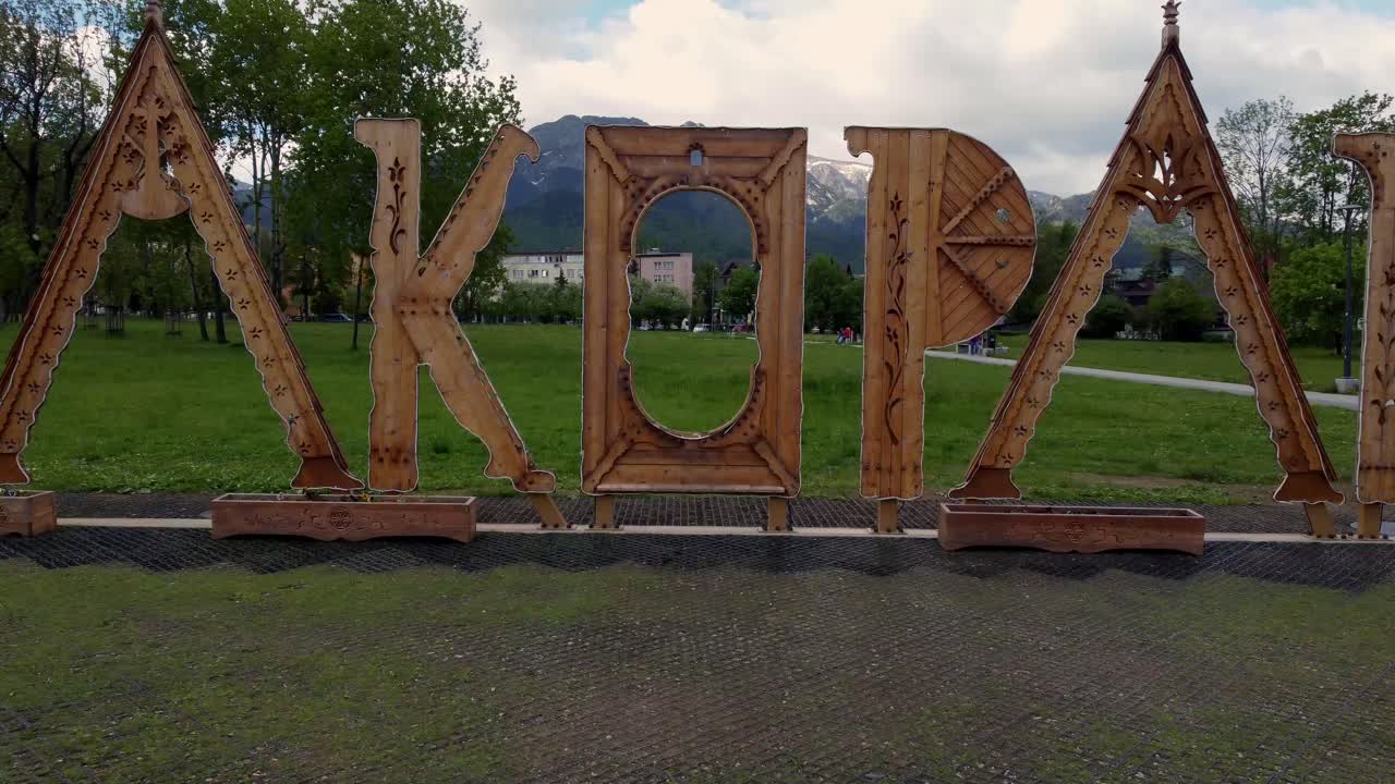 знаменитый деревянный знак закопане возле польского татри горы, сельскохозяйственные угодья, леса, пасмурное небо и легендарный пик гевонт возле закопане, польша, курортного города с традиционной горальской архитектурой - 4k 30fps-1