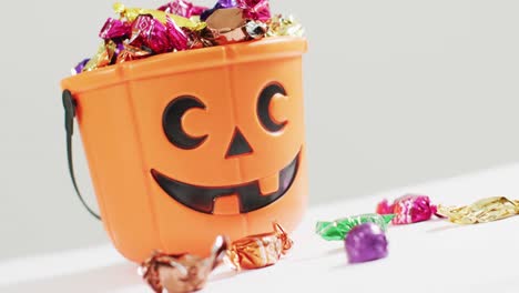 scary halloween pumpkin printed bucket full of candies against grey background