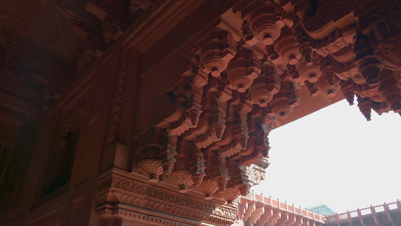 Pengambilan gambar close-up sudut rendah statis braket ornamen batu pasir merah berukir rumit di Jahangiri Mahal di dalam Benteng Agra di Uttar Pradesh, India