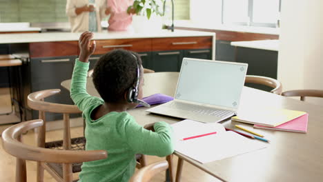 african american boy having online class using headphones and laptop with copy space, slow motion