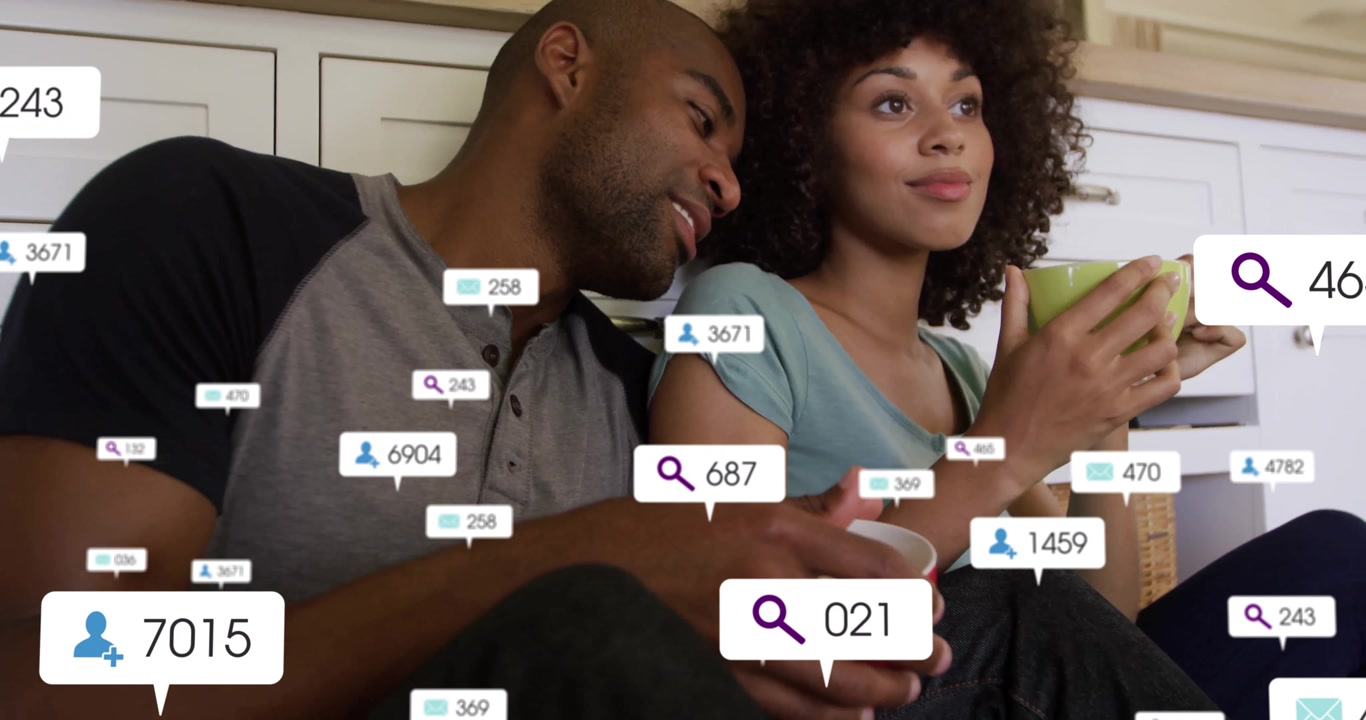 Man and woman entering kitchen holding mugs as social icons popping up around man leaning closer