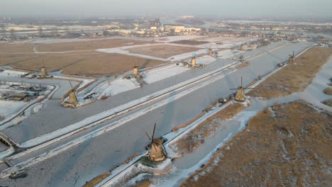 Sunrise-at-iconic-Dutch-windmills-during-cold-winter-with-frozen-river,-aerial