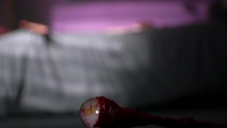 globo ocular, cubierto de sangre, en el suelo, con la pupila mirando a su alrededor, en un estilo de película de terror vfx tiro de bajo ángulo y la víctima retorciéndose en el fondo en la cama