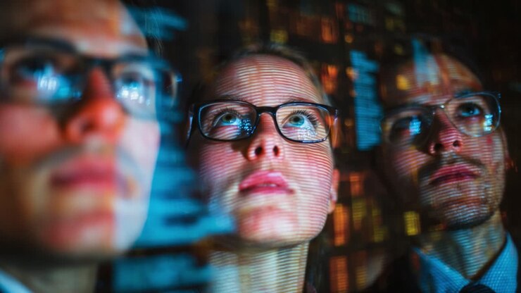 Focused Group of Professionals Analyzing Data Projections in a High-Tech Environment with Visibly Captivated Expressions and Digital Displays Reflected on Their Glasses