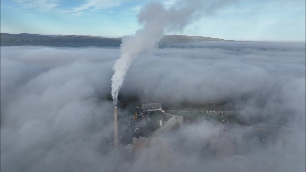 Ciminiera di una fabbrica di cemento sopra la nebbia in città