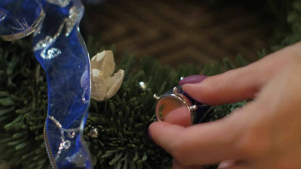 Donna che crea una corona d'Avvento in abete per la Vigilia di Natale e la decora con un piccolo rullante blu, decorazione artigianale fai da te, tradizioni invernali, festività stagionali, ripresa ravvicinata delle mani.
