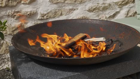 Fire-burning-in-a-round-cast-iron-fire-pit-in-front-of-a-stone-wall,-close-up-shot