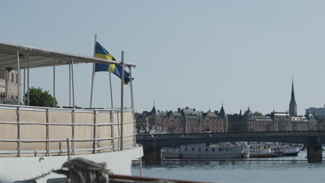 swedish flag moves in wind on boat, stockholm skyline in background