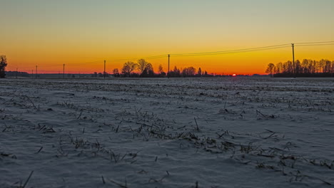 a golden dawn as the sunrise illuminates a farmland field covered in snow - time lapse