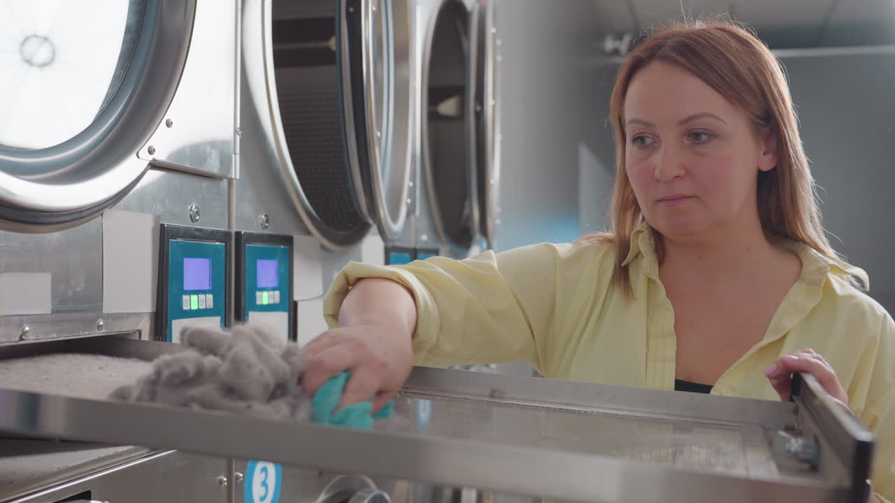 Laundry owner uses towel to clean lint dirt from washer filter, maintaining hygiene and efficiency of industrial laundromat machines during routine service, ensuring smooth performance