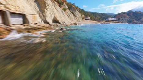 FPV-Drohne-Fliegt-Schnell-An-Einem-Strand-Entlang,-Vorbei-An-Bootshäusern-An-Der-Malerischen-Küste-Spaniens