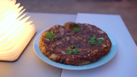 top view of a traditional homemade spanish omelette 'tortilla' with eggs, fried potato and vegetables, garnished with freshly chopped parsley leaves and served on a white plate.