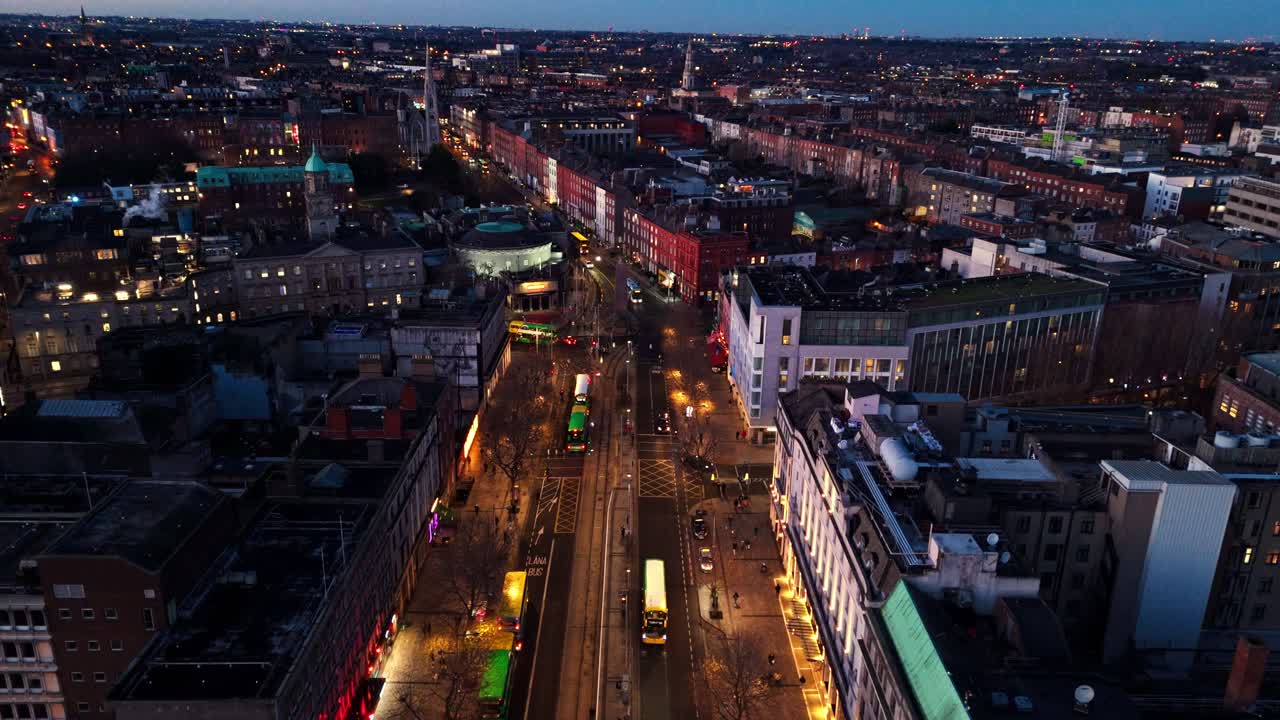 aerial landscape drone shot flying down O'Connell street in Dublin Ireland at winter nighttime with Irish cityscape buildings and illuminated roads and cars and tourists below exploring the night