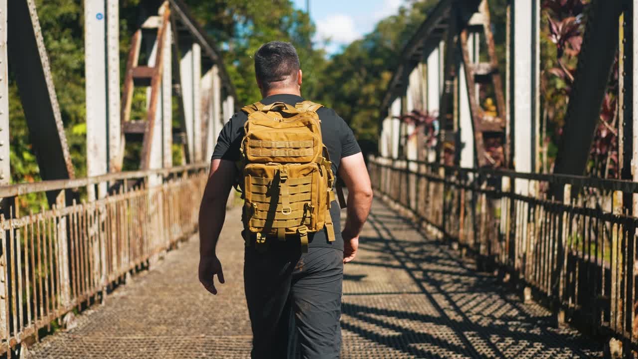 joven viajero con mochila caminando por el viejo puente oxidado al aire libre en un soleado día de verano