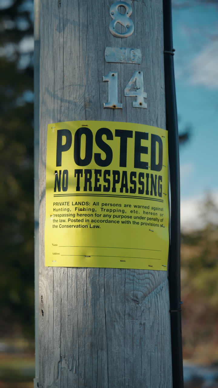 Bright yellow no trespassing notice attached to wooden utility pole, private land warning sign restricting entry in outdoor rural area