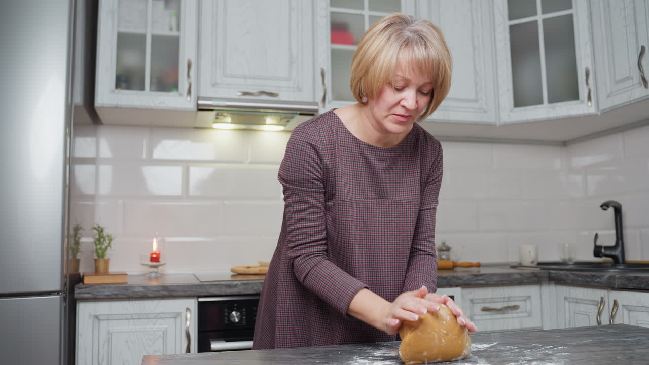 молодая леди выпекает свежее тесто на кухонном столе, готовит домашние выпечки, современную кухню с белыми шкафчиками, посудой и теплым освещением