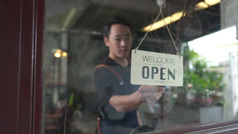 4k asian man coffee shop owner turning hanging closed sign to open on the door