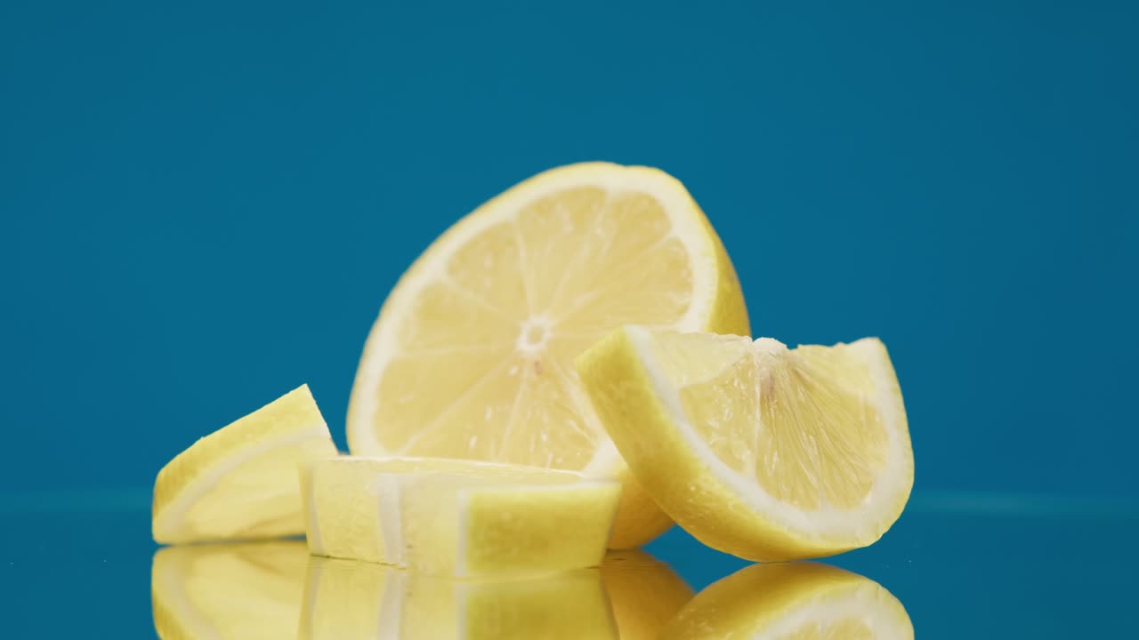 primer plano de piezas de limón maduras giratorias sobre un fondo azul, haciendo un cóctel de cítricos, bebiendo limonada fría, disparando frutas frescas en rodajas