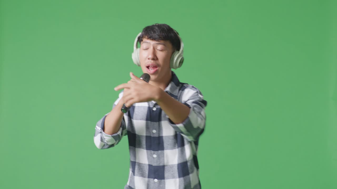 젊은 아시아 십대 소년이 마이크를 들고 녹색 화면 배경에서 을 연주하고 있습니다.