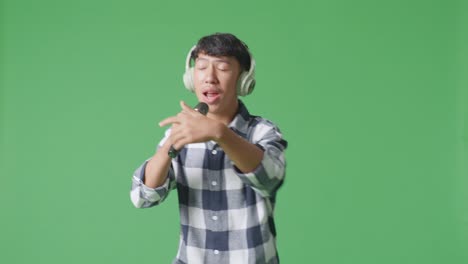 젊은 아시아 십대 소년이 마이크를 들고 녹색 화면 배경에서 을 연주하고 있습니다.