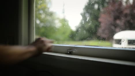 person closing a white wooden window locking it with a chrome metal lever