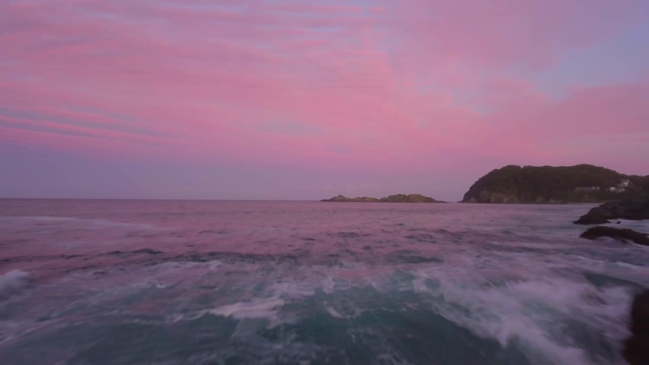 Ascending Aerial flyover sandy beach and rocks with the ocean in background during pink sky after sunset. Seal rocks Australia.
