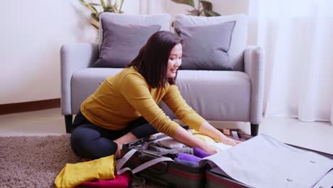 asian woman arranging clothes in takeout suitcase in her living room