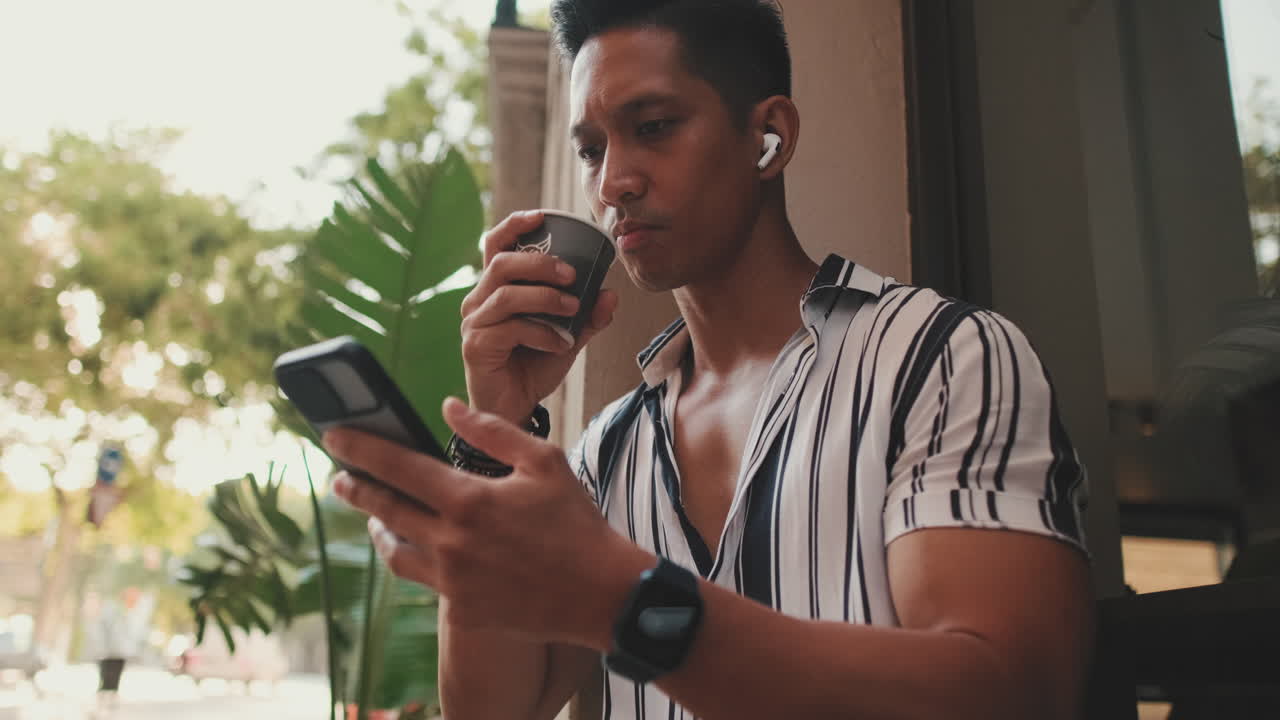 Man using phone and drinking coffee at cafe