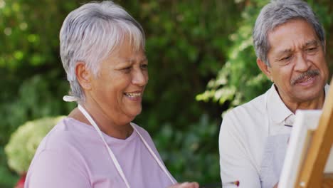 video of happy biracial senior couple painting in garden