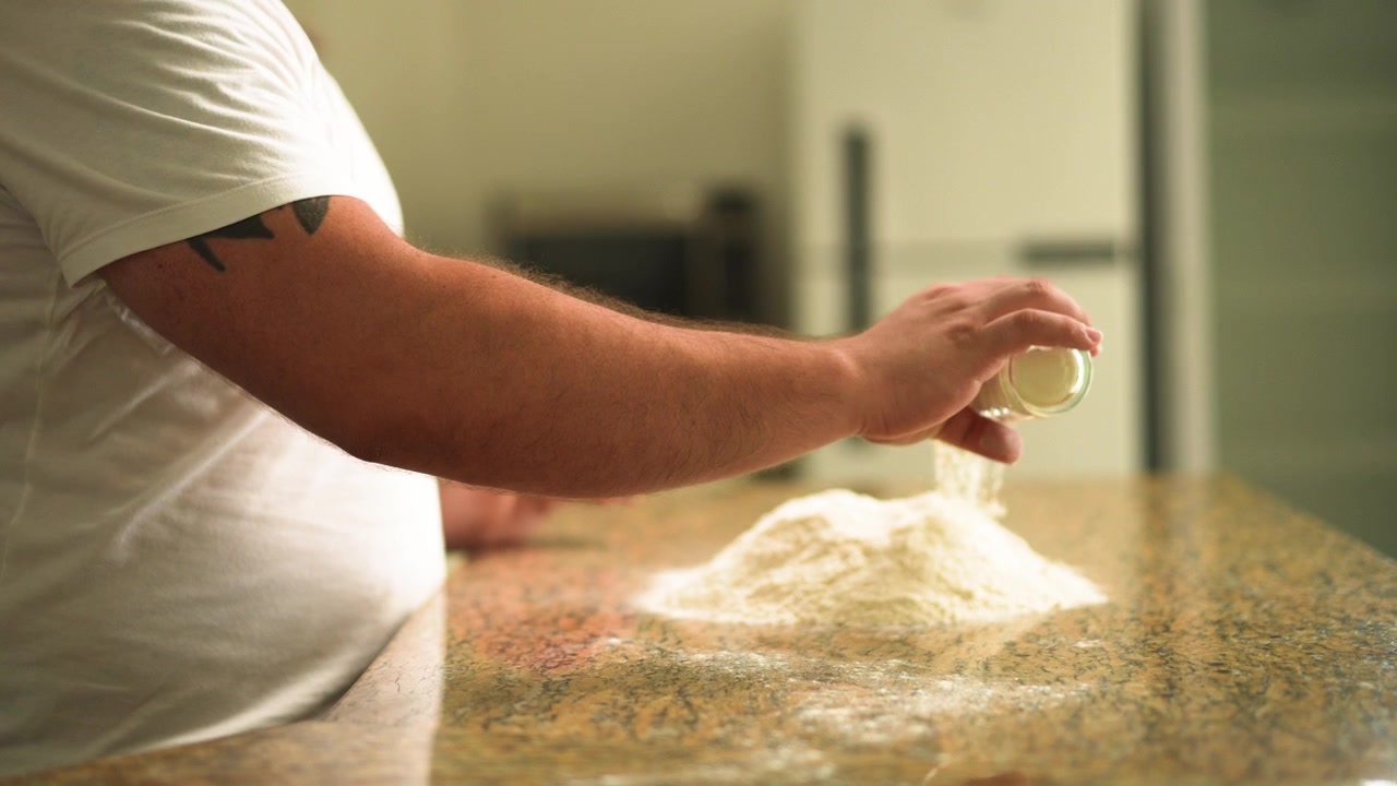 Le mani dello chef iniziano a preparare l'impasto della pizza versando farina fresca su una superficie della cucina