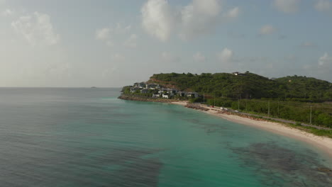 aerial zoom in view beautiful luxury property complex homes in antigua and bermuda caribbean coast with turquoise water and sandy beach in sunny day