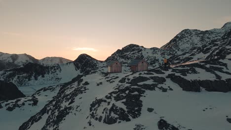 person is standing behind two wooden huts at sunrise in the austrian alps