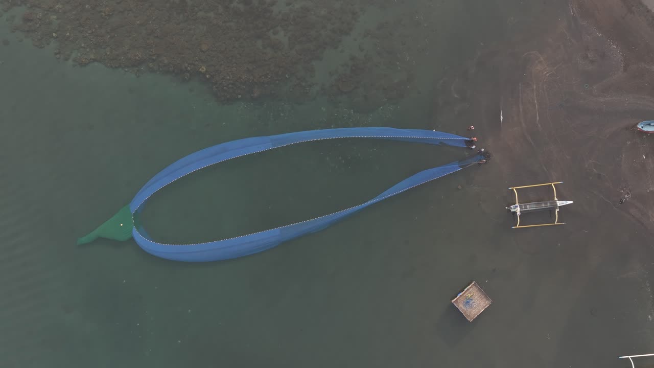 Aerial of group pulling large fishing net on shore in Indonesia