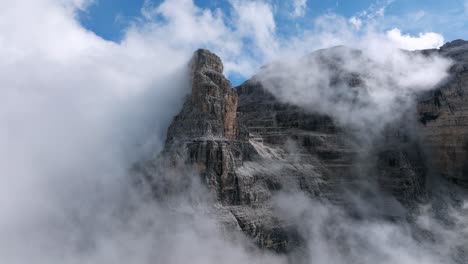 volo aereo con drone che mostra gigantesche montagne rocciose con cime circondate da nuvole - dolomiti di brenta in italia