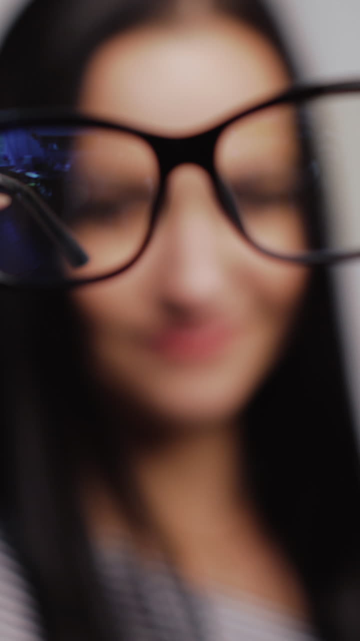 Fashionable eyeglasses close-up on the blurred background of a woman. Woman shows and then puts on new glasses in black rim. Vertical video