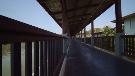 A-boardwalk-along-a-tropical-river-running-through-a-village-in-Thailand---sliding-view