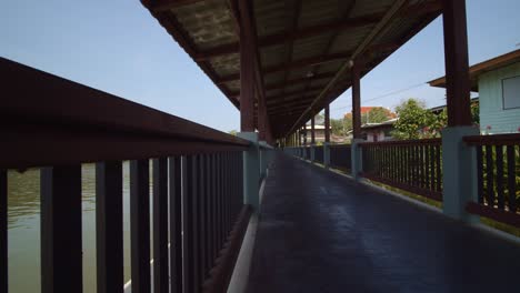 a boardwalk along a tropical river running through a village in thailand - sliding view